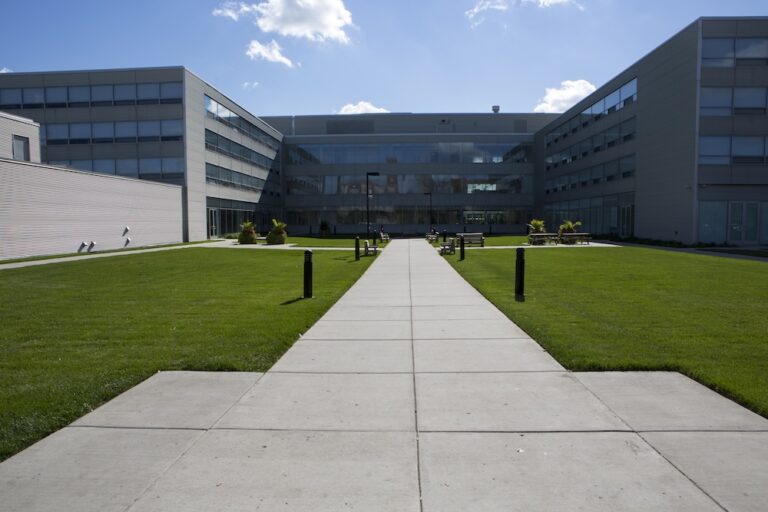 View of a large facility with a green lawn and wide sidewalk leading up to the entrance