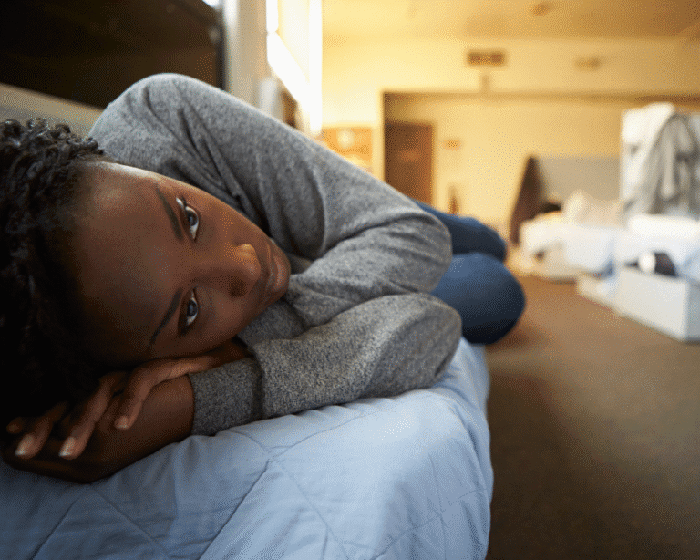Young woman lying on a cot looking thoughtful in a shared shelter space