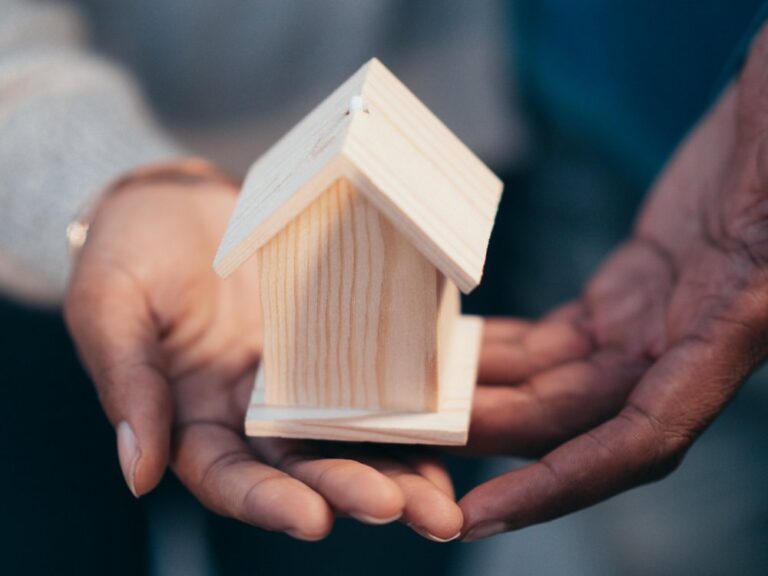 Hands holding a small wooden house model