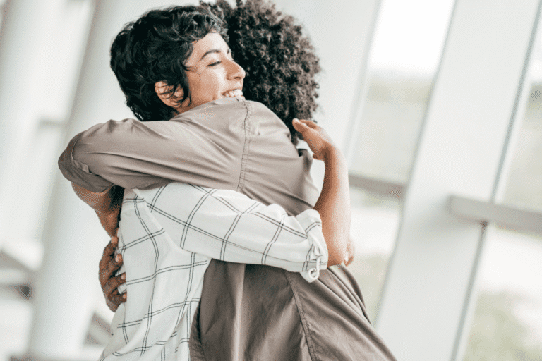 Two people hugging in front of large windows