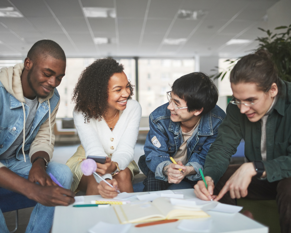 Group of diverse young adults sitting in a circle smiling and writing.