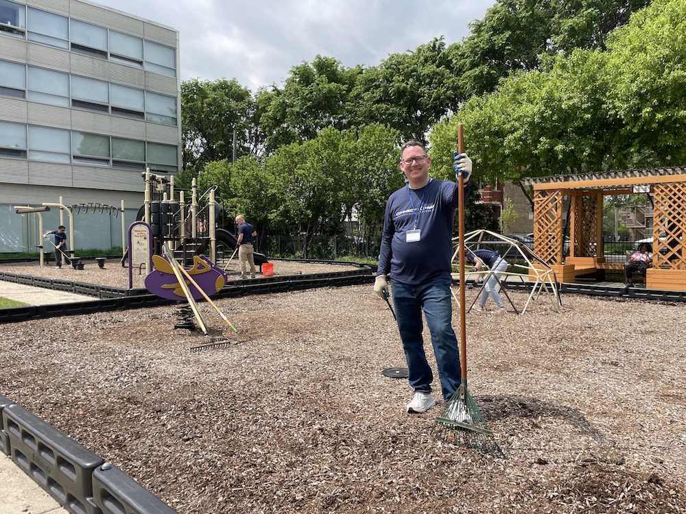Volunteer with a rake working in a playground area.