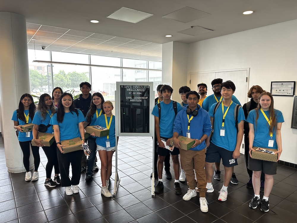 Group of students in blue shirts holding boxed lunches inside lobby.