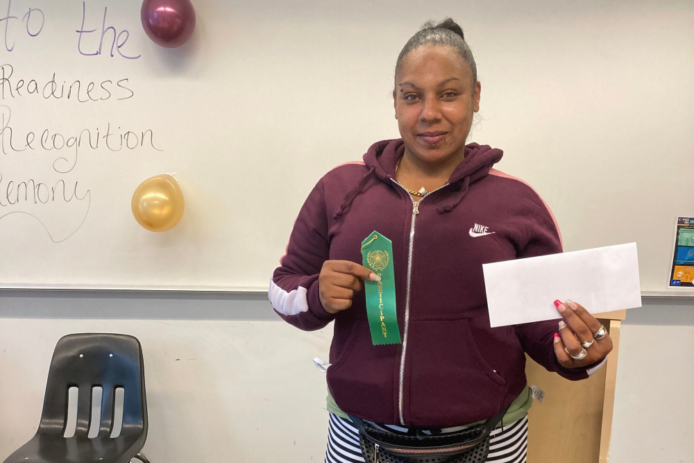 Woman holding a ribbon and envelope at a job readiness recognition ceremony.