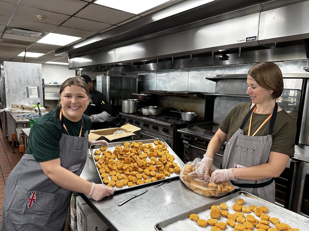 Two volunteers preparing food in a commercial kitchen