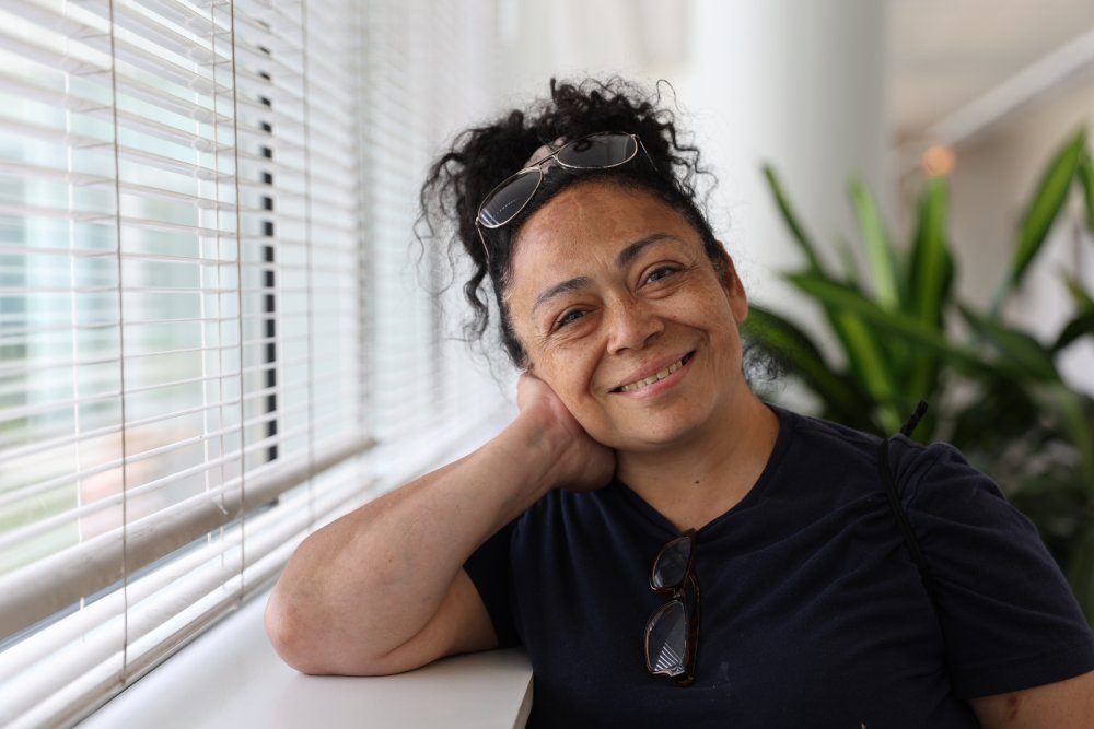 Smiling woman sitting beside a window with her head resting on her hand.