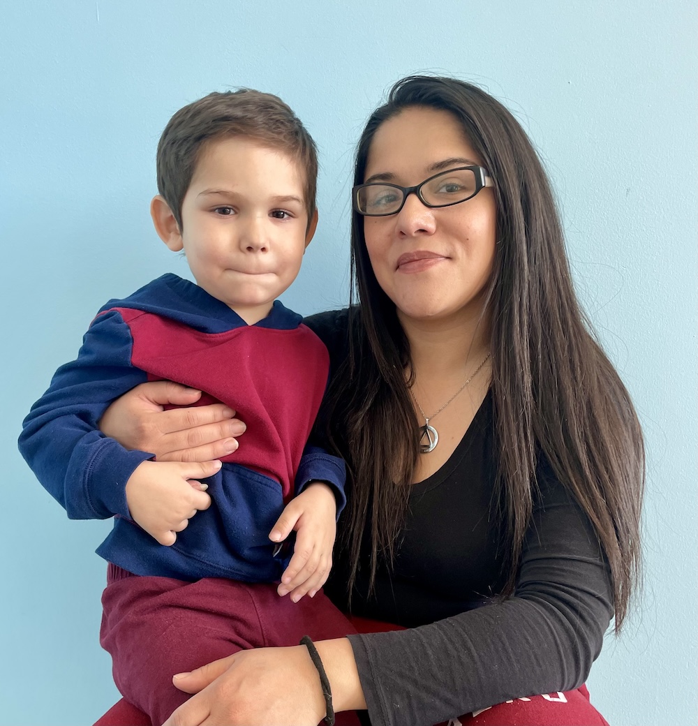 Mother with glasses smiling while holding her young son in front of a blue wall