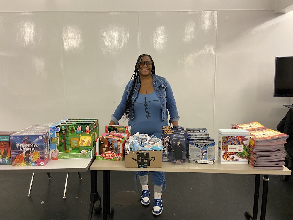 Woman standing behind a table filled with holiday toys and books for donation.