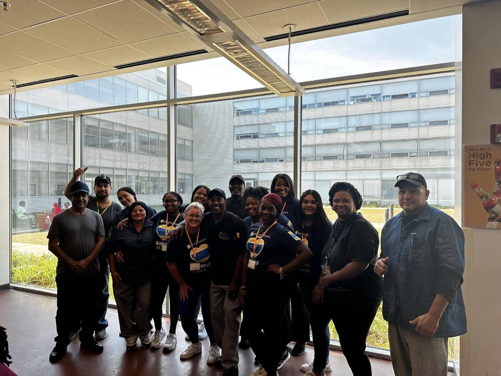 Large group of volunteers smiling indoors in front of large windows.