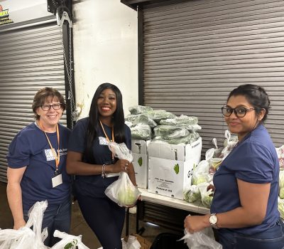 Three volunteers smiling while packing fresh produce