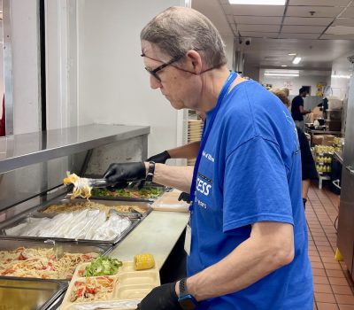 Older volunteer serving food at cafeteria-style station