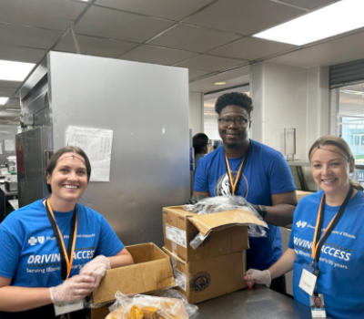 Three BCBSIL employees volunteering in the A Safe Haven Foundation kitchen, smiling while packaging meals.