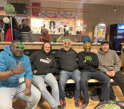 Group of men smiling and wearing festive glasses at a bowling alley