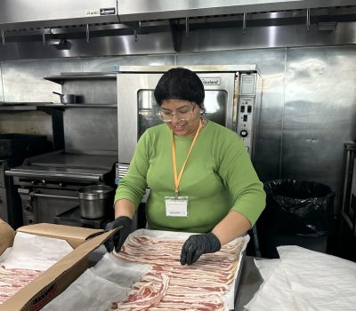 Woman in green shirt preparing bacon in a commercial kitchen