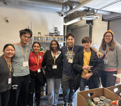 Group of young volunteers in front of a shelf full of canned goods