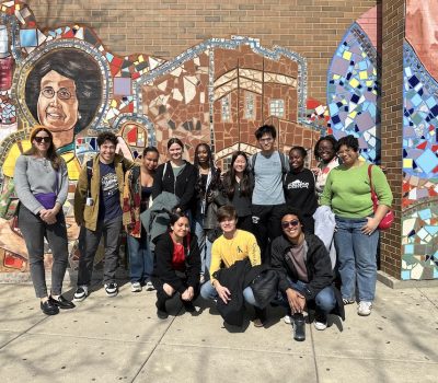 Group of volunteers standing outside in front of a colorful mosaic wall
