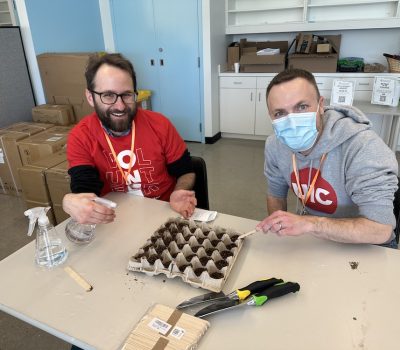 Two men preparing seed trays at a table with gardening tools