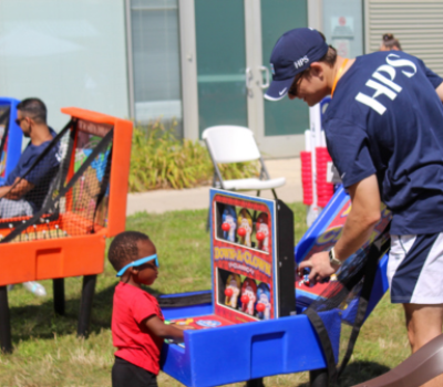 Volunteer and small child playing arcade basketball at outdoor event