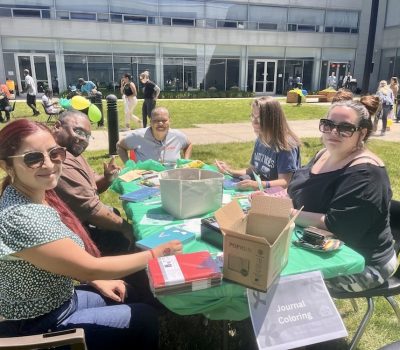 Group of people smiling and participating in a journal coloring activity outdoors.