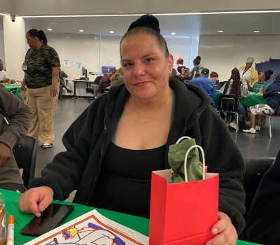 Woman smiling and holding a gift bag with coloring sheets in front of her.