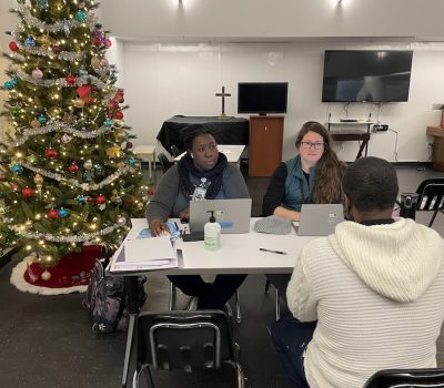 Two staff members assisting a client at a holiday-decorated intake station