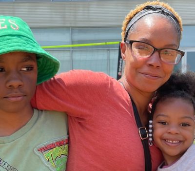 Mother hugging her two children outdoors in front of a modern building