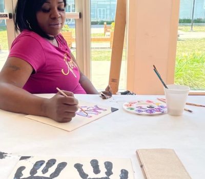 Woman painting with colorful paints and a canvas showing her handprints.