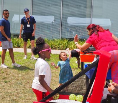 Children playing a ball toss game while adults cheer them on.