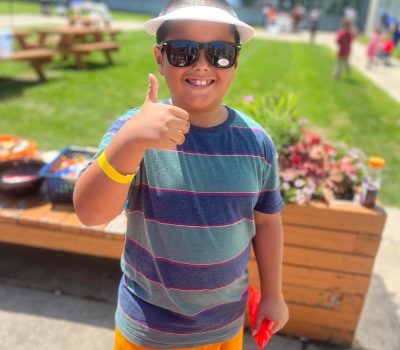 Smiling boy wearing sunglasses and giving a thumbs-up.