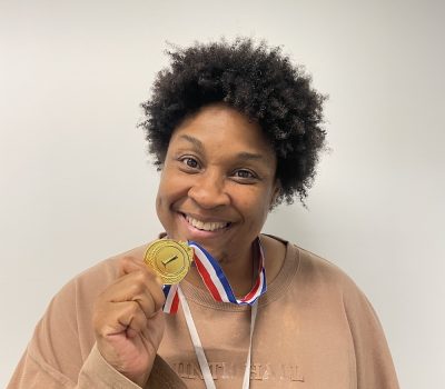 Smiling woman holding a gold medal.