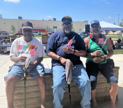 Three veterans sitting together, each holding a small American flag.