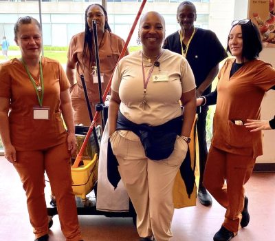 Group of women in custodial uniforms smiling with cleaning equipment
