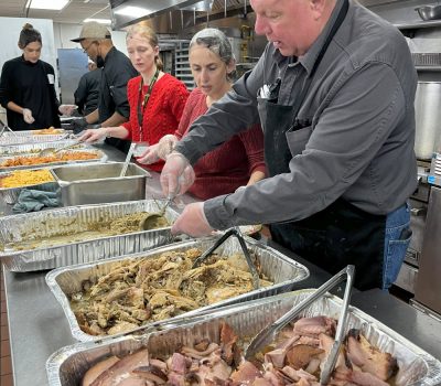 Staff volunteering on Thankgiving serving holiday food in a kitchen with trays of meat and sides